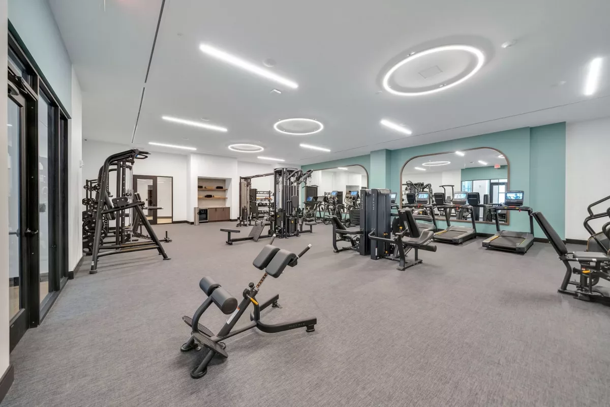 Fitness center with treadmills, weight machines, and mirrored wall. Gray carpet flooring.