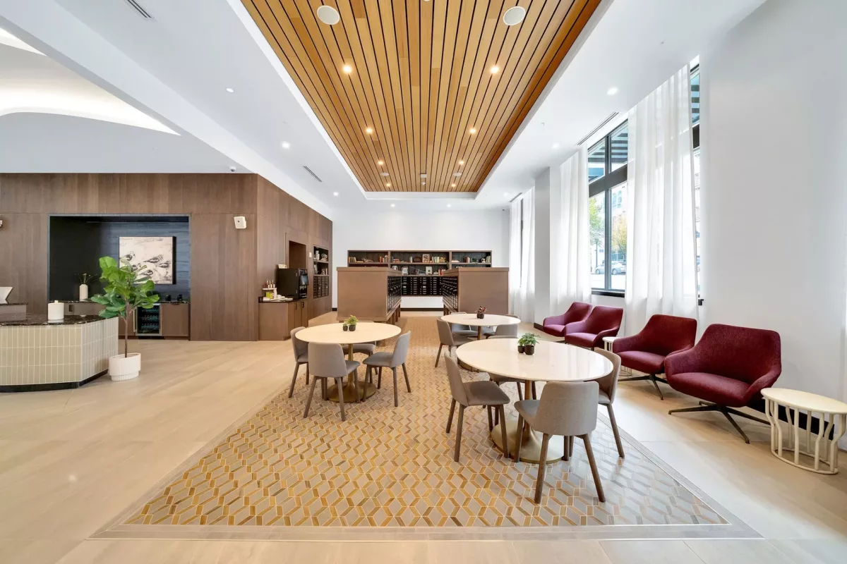 Lounge area with tables, chairs, wood ceiling, and large windows with sheer white curtains.