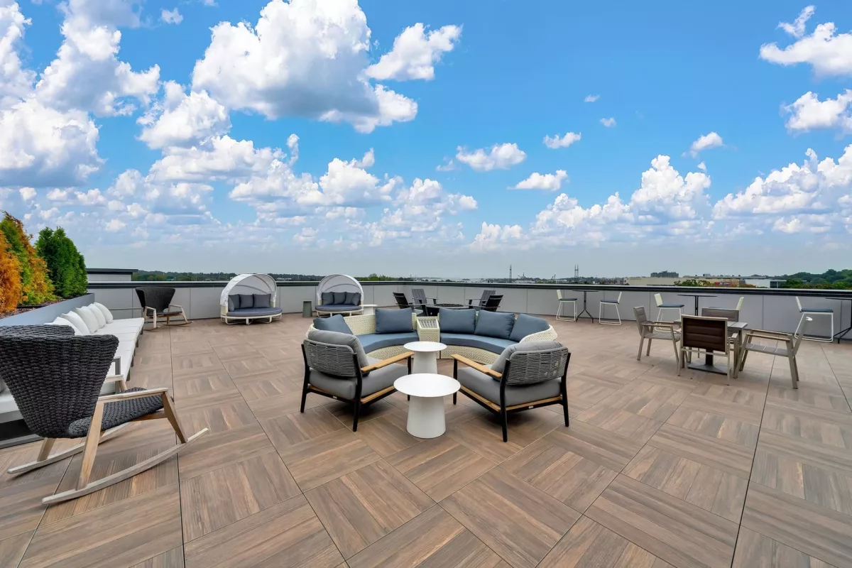 Rooftop lounge with seating, tables, and city views under a blue sky.