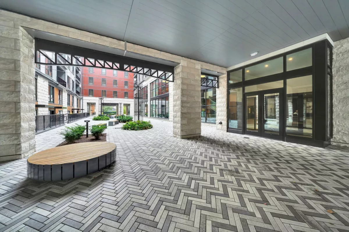 Covered courtyard with herringbone brick, stone pillars, wood bench, and building views.
