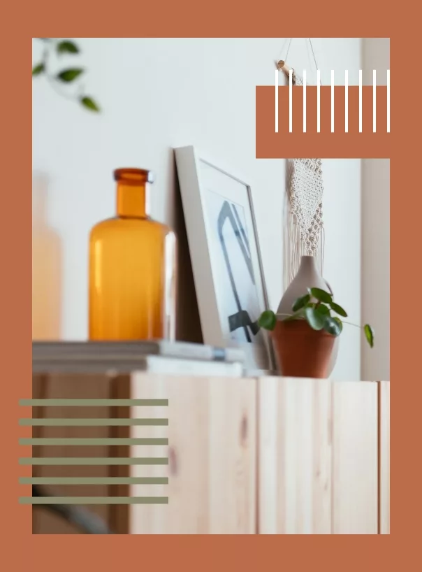 Minimalist decor with a wooden cabinet, amber bottle, potted plant, and macrame on a terracotta background.